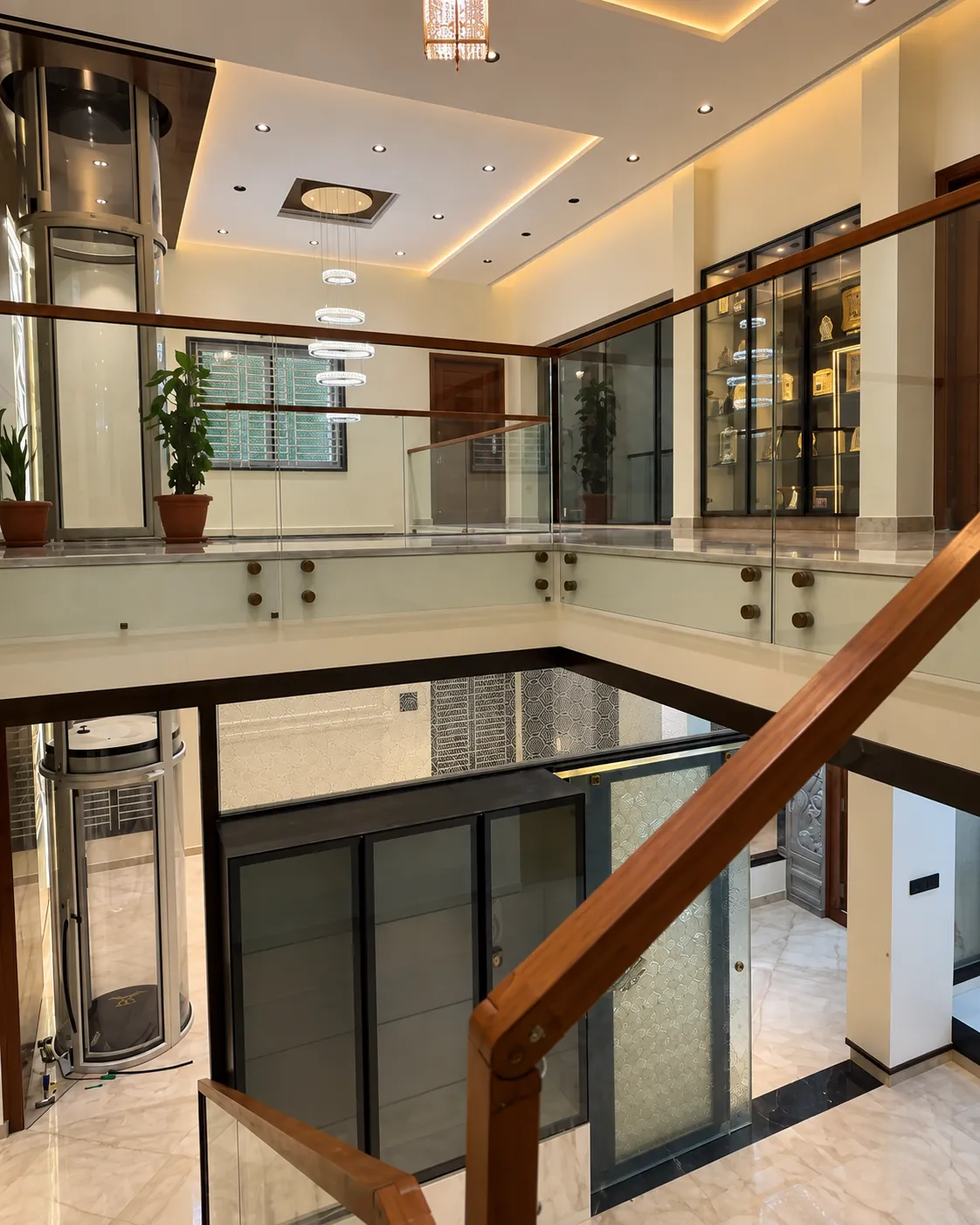 Glass elevator and wooden staircase railing inside an SJ Infra-built home